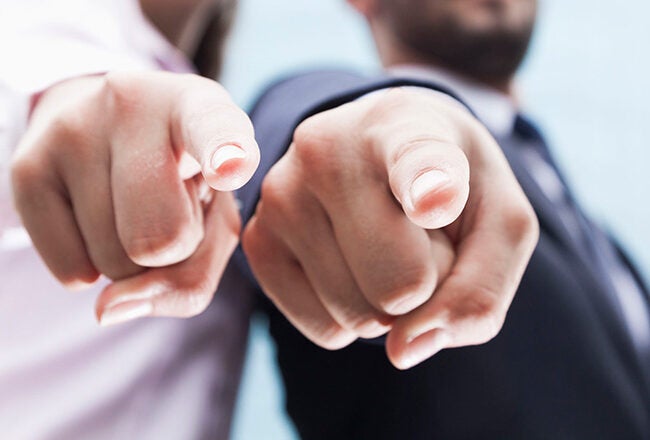 Two people in business attire pointing towards the camera, suggesting recruitment, selection, or direct engagement.