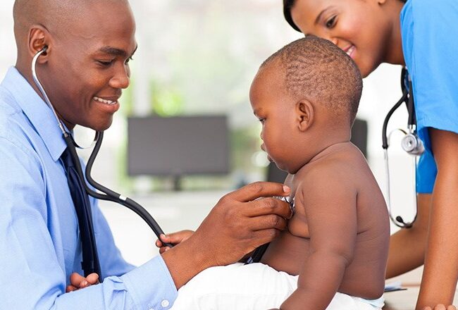 A healthcare professional listens to a baby''s chest with a stethoscope while another healthcare worker smiles. It represents pediatric healthcare.