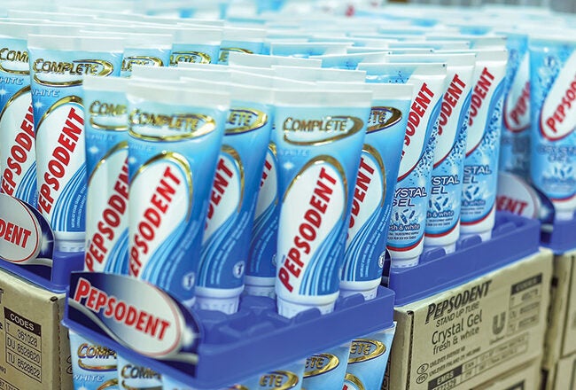 Tubes of Pepsodent toothpaste displayed on shelves in a store setting, with boxes stacked below.