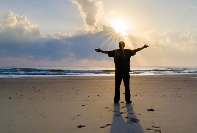 A person standing on a beach with arms outstretched towards the sunrise, symbolizing freedom or tranquility.