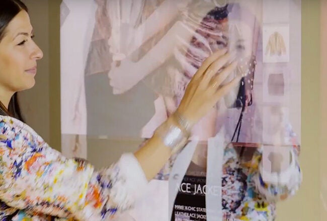 A person interacting with a digital touch screen displaying fashion content, indicating the use of technology in fashion retail.
