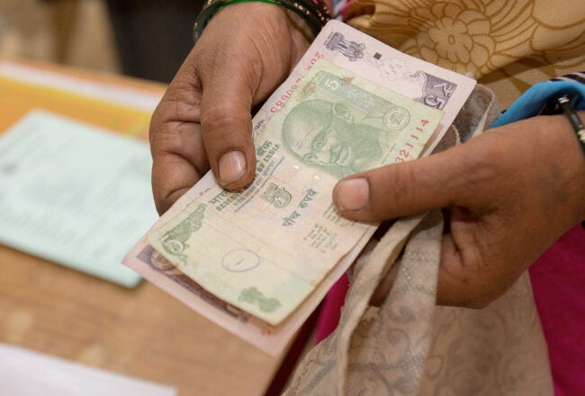 A person holding Indian currency notes with a partially visible document in the background.