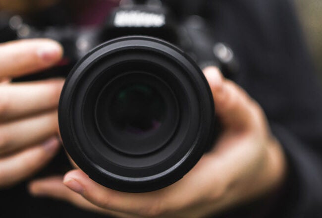 Close-up of a person holding a camera with a large lens, focusing on the lens itself.