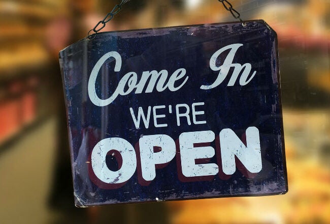 A sign hanging in a shop window that reads, "Come In We''re Open," indicating the business is open to customers.