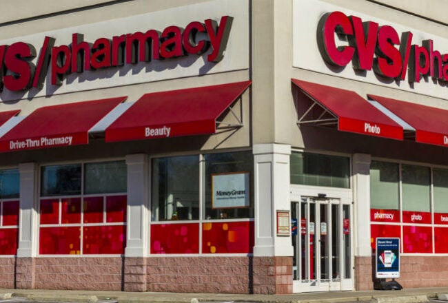 The image shows the exterior of a CVS Pharmacy store, featuring red awnings and signage reading "CVS/pharmacy" on a brick building.