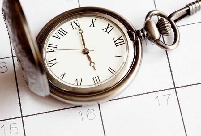 A pocket watch with Roman numerals rests on a calendar, symbolizing the concept of time management or planning.