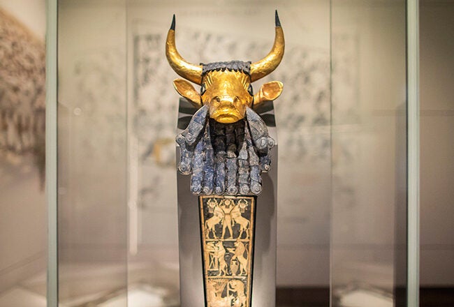 A gold and blue statue of a bull''s head with large curved horns, adorned with intricate details, displayed in a museum exhibit.