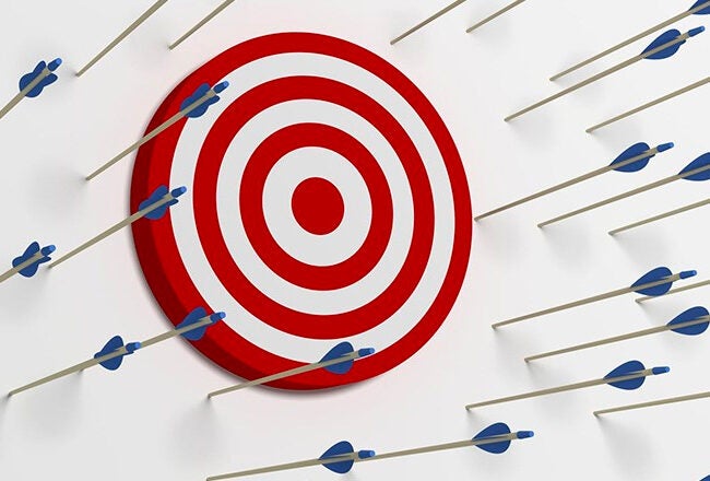 A target with red and white circles is on a wall surrounded by numerous arrows missing the bullseye, representing failure or missed opportunities.