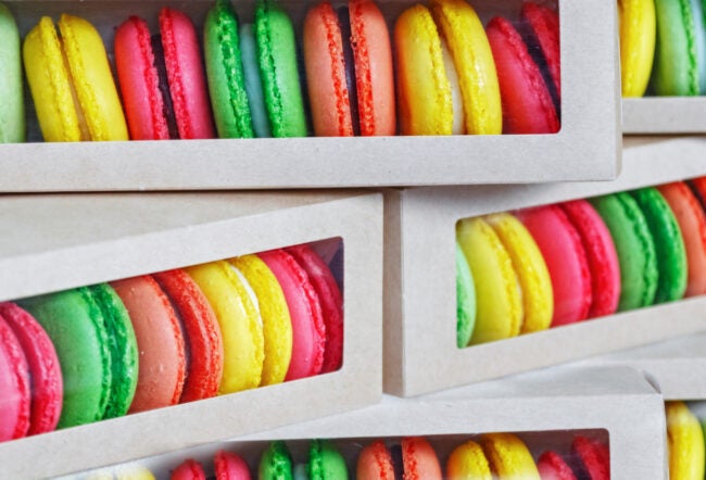 Colorful macarons packed in cardboard boxes with transparent windows, showcasing a variety of vibrant hues like yellow, green, and red.