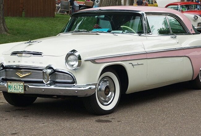 A vintage white and pink DeSoto Fireflite car parked on a street, featuring chrome details and classic design elements from the 1950s.