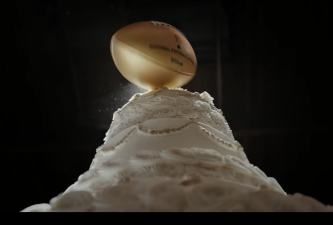 A tiered wedding cake topped with a golden football, symbolizing the combination of a wedding and sports theme.