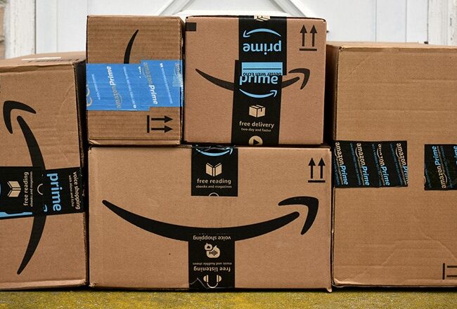 Several Amazon Prime cardboard boxes stacked in front of a house door, symbolizing online shopping and delivery services.