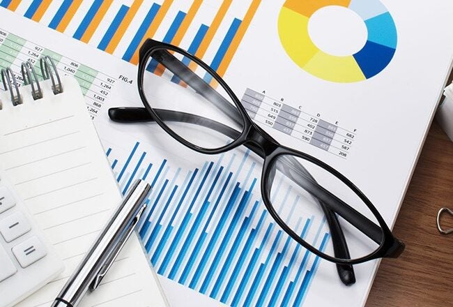 Calculator, notepad, pen, eyeglasses, and data charts with graphs and pie charts on a desk, symbolizing financial analysis.