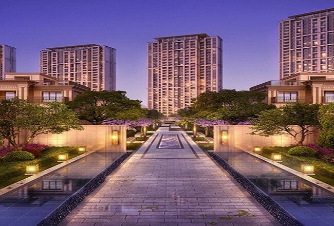 A luxurious residential complex featuring modern high-rise buildings and lower traditional-style buildings, with landscaped gardens and a long pathway lined with water features and lanterns.