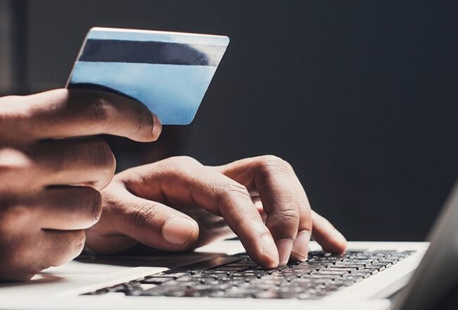 A person holding a credit card while typing on a laptop keyboard, representing online shopping or digital transactions.