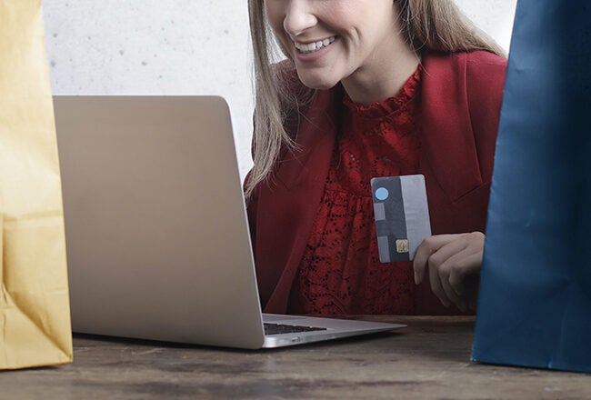 A person shopping online using a laptop, holding a credit card, with shopping bags in the foreground, representing online shopping.