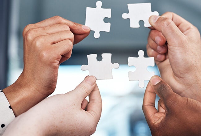 Four hands holding interlocking puzzle pieces, symbolizing teamwork and collaboration.