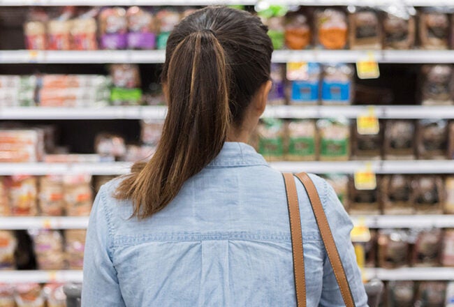 A person with their back to the camera is standing in a grocery store, looking at shelves filled with various types of packaged bread.