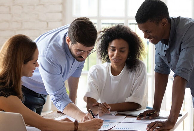 A diverse group of four people collaboratively working around a table, looking at documents and graphs, representing teamwork and brainstorming.