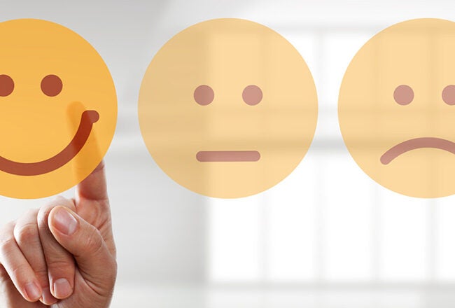 A hand is pointing at a happy face icon among neutral and sad face icons, representing a choice of positive emotion or feedback.