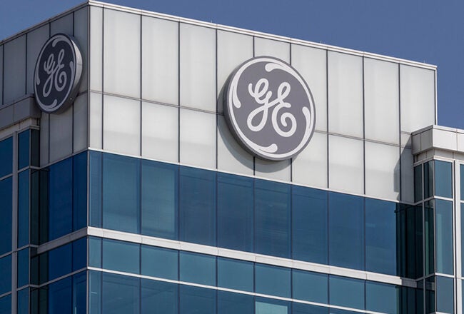 A modern office building with a large GE logo on the top corner against a clear blue sky.