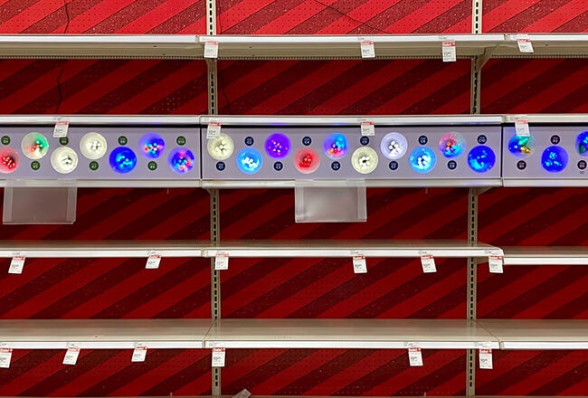 Empty store shelves with a display of various colorful holiday-themed light bulbs above.