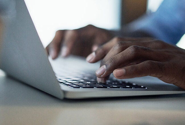 A person typing on a laptop, representing technology use or remote work. Hands are on the keyboard in a focused environment.