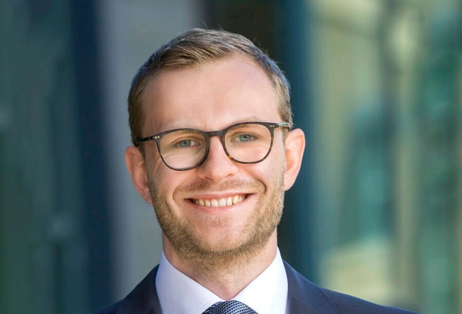 Headshot of a person wearing glasses and a suit, smiling, with a blurred background.