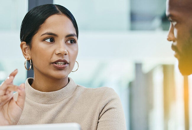 Two people engaged in a discussion in a modern office setting, one gesturing as they speak.