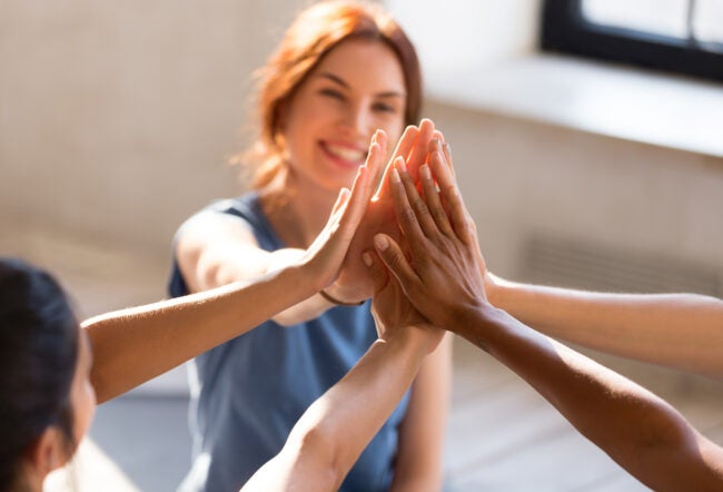 A group of people high-fiving, symbolizing teamwork and unity. One smiling person is visible in the background.