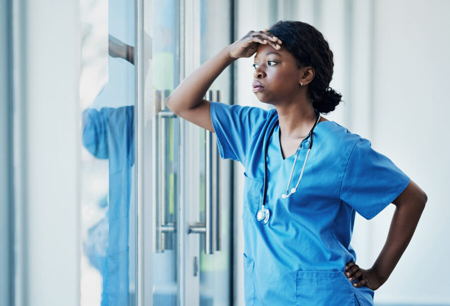A nurse struggling with burnout and shift work standing inside a hospital