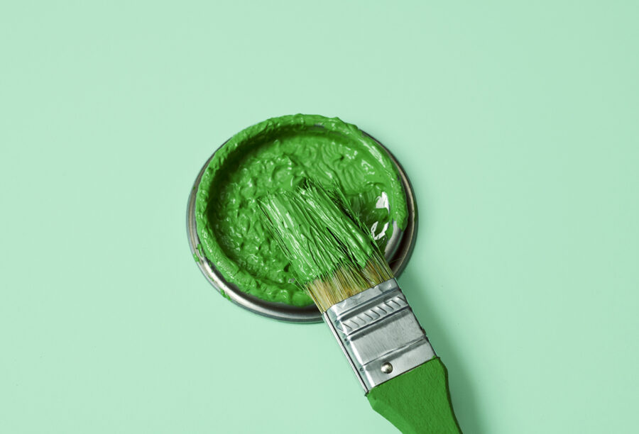Paint brush dipping into green paint to symbolize companies greenwashing and misrepresenting green stocks