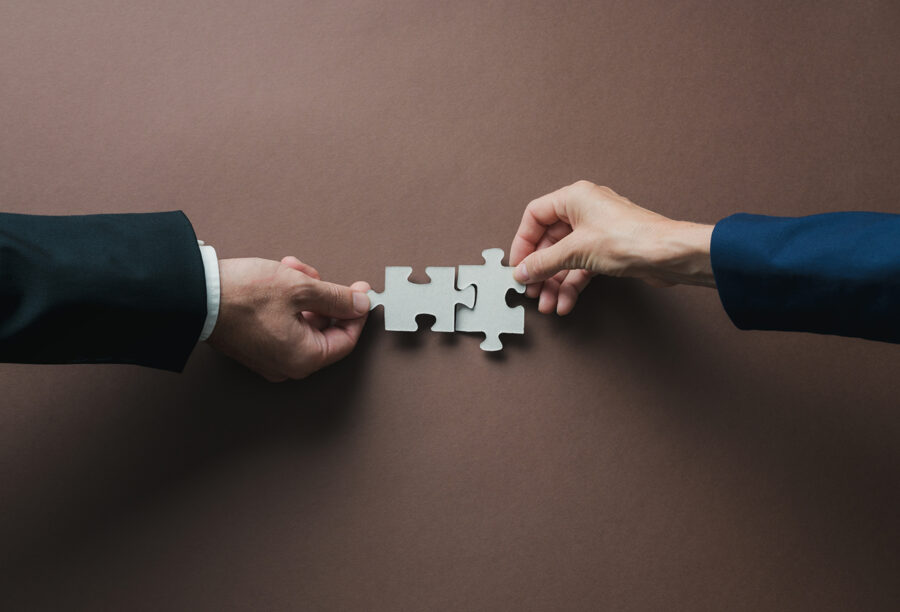 Two hands putting puzzle pieces together to represent business mergers and acquisitions