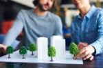 Office workers putting trees on an architectural model to show how businesses are dealing with corporate social responsibility and ESG investing