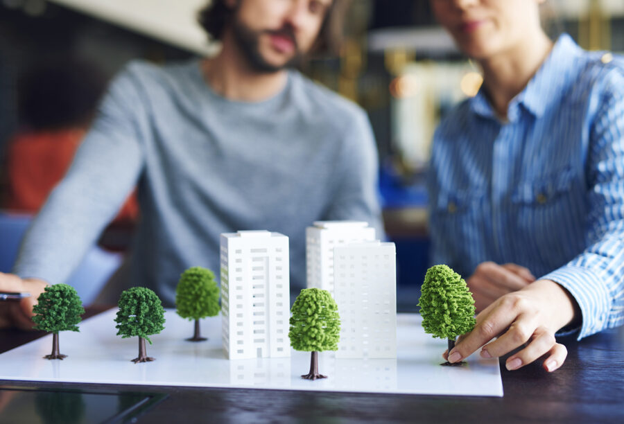 Office workers putting trees on an architectural model to show how businesses are dealing with corporate social responsibility and ESG investing