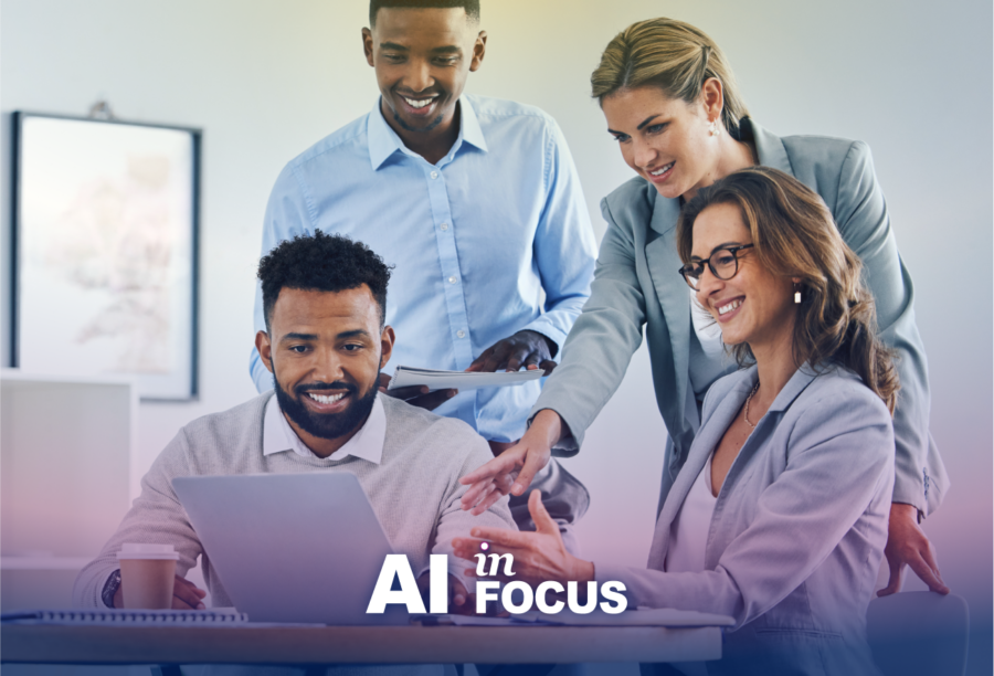A group of diverse employees looking at a laptop to show how AI can make you a better manager with a text overlay that reads "AI in Focus"