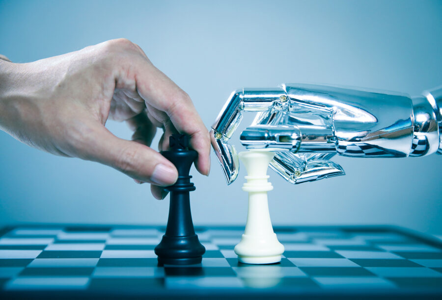 A human hand and a robot hand placing chess pieces on a chessboard to show how training with AI can improve human performance
