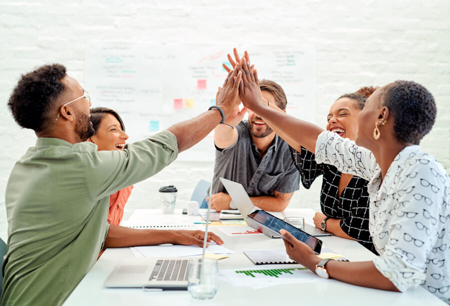 Group of employees who are engaged at work high-fiving over a conference table