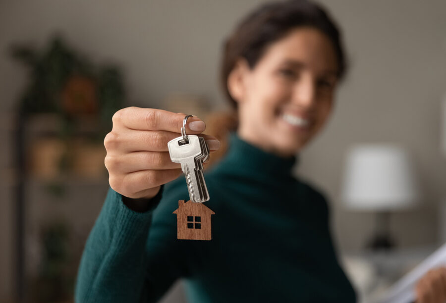 A smiling woman real estate agent holds out a set of house keys to show that the market is predicted to look up in 2024
