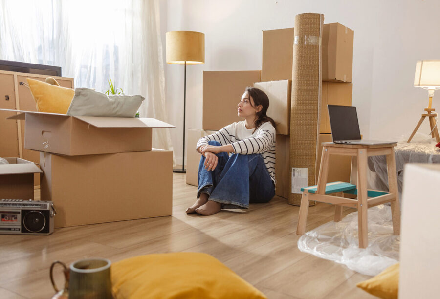 Young woman sitting in an apartment surrounded by moving boxes. Will Gen Z be able to afford houses?