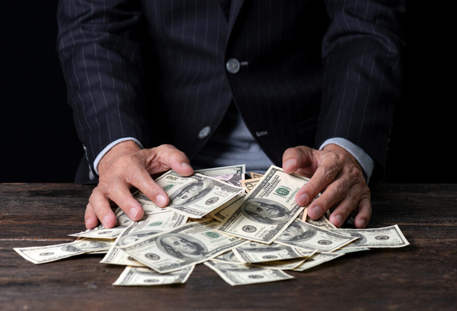 Business man in a suit gathering a pile of cash on a table with his hands