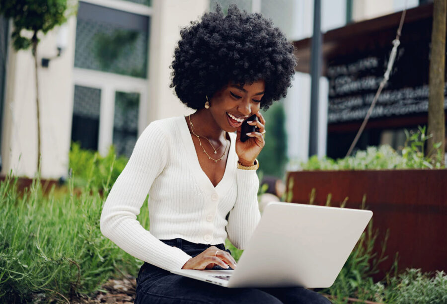 Black entrepreneur smiling on the phone as she uses her laptop
