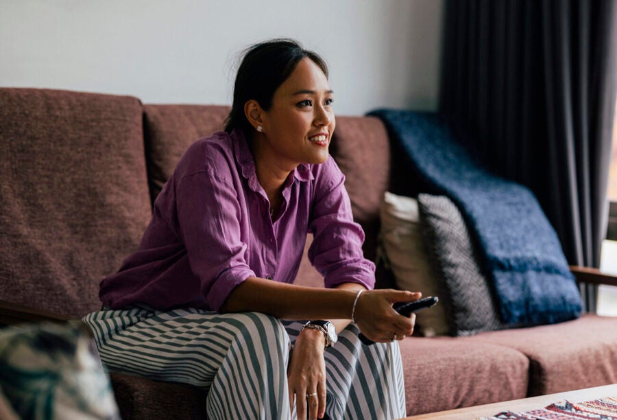 Woman of color sitting on the couch with a remote and watching TV to show that representation in marketing matters