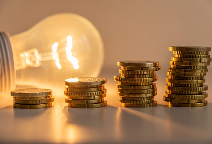 Stacks of coins in front of a lightbulb to show how financial frictions affect innovation