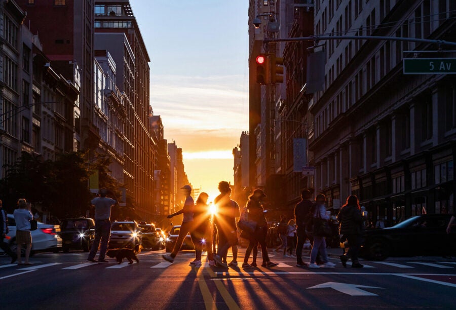 Sun setting behind pedestrians crossing the street in NYC to show how foreign income tax affects U.S. workers