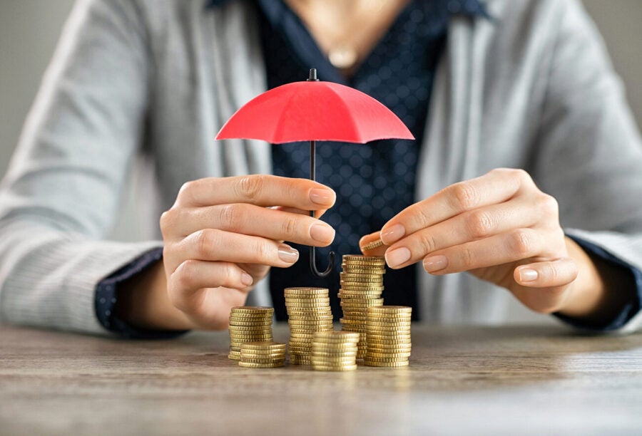 Person's hands holding a small umbrella over a pile of coins to show how optimal deposit insurance can help prevent bank runs