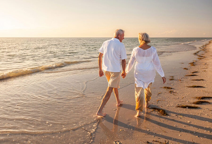 Retired elderly couple walking on the beach at sunset.