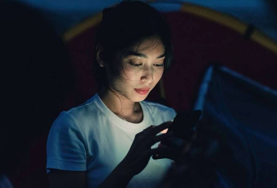 Woman looking thoughtfully at her phone in a dark room. Who Benefits in the Deal Between Reddit and OpenAI?