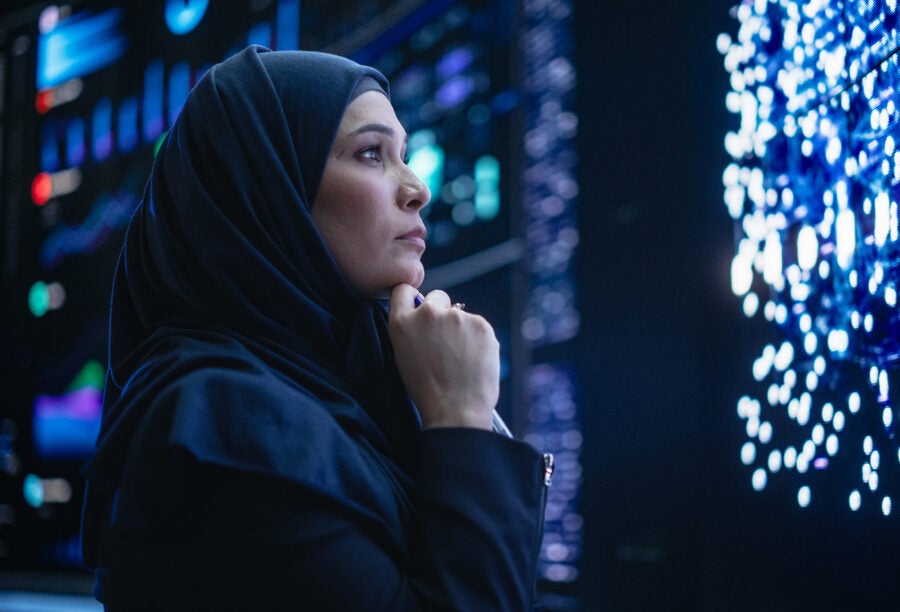 Woman gazing thoughtfully at a large digital screen. How can we harness AI to fulfill our potential?