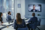 Employees in a conference room having a meeting with a virtual team member on a screen